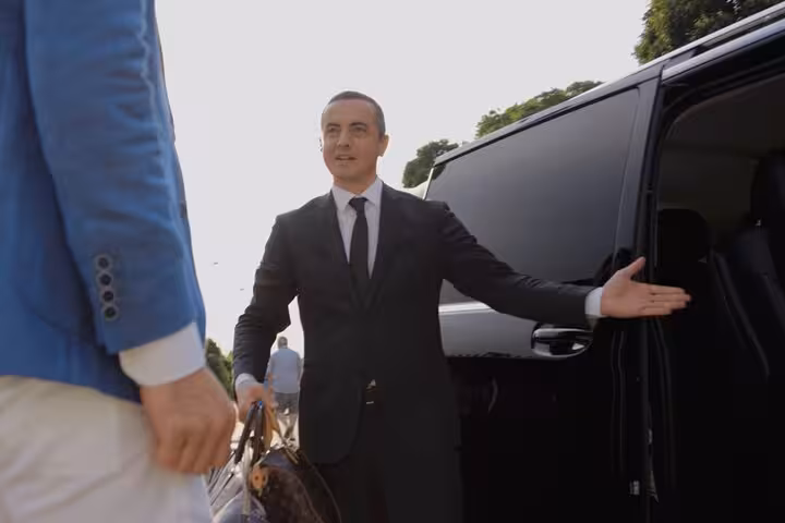 Chauffeur welcoming passenger into luxury van for Cortina d'Ampezzo to Venice transfer, ensuring comfort.