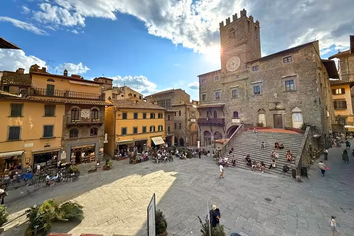 Scenic view of the historic Piazza della Repubblica in Cortona, bustling with people under a blue sky.