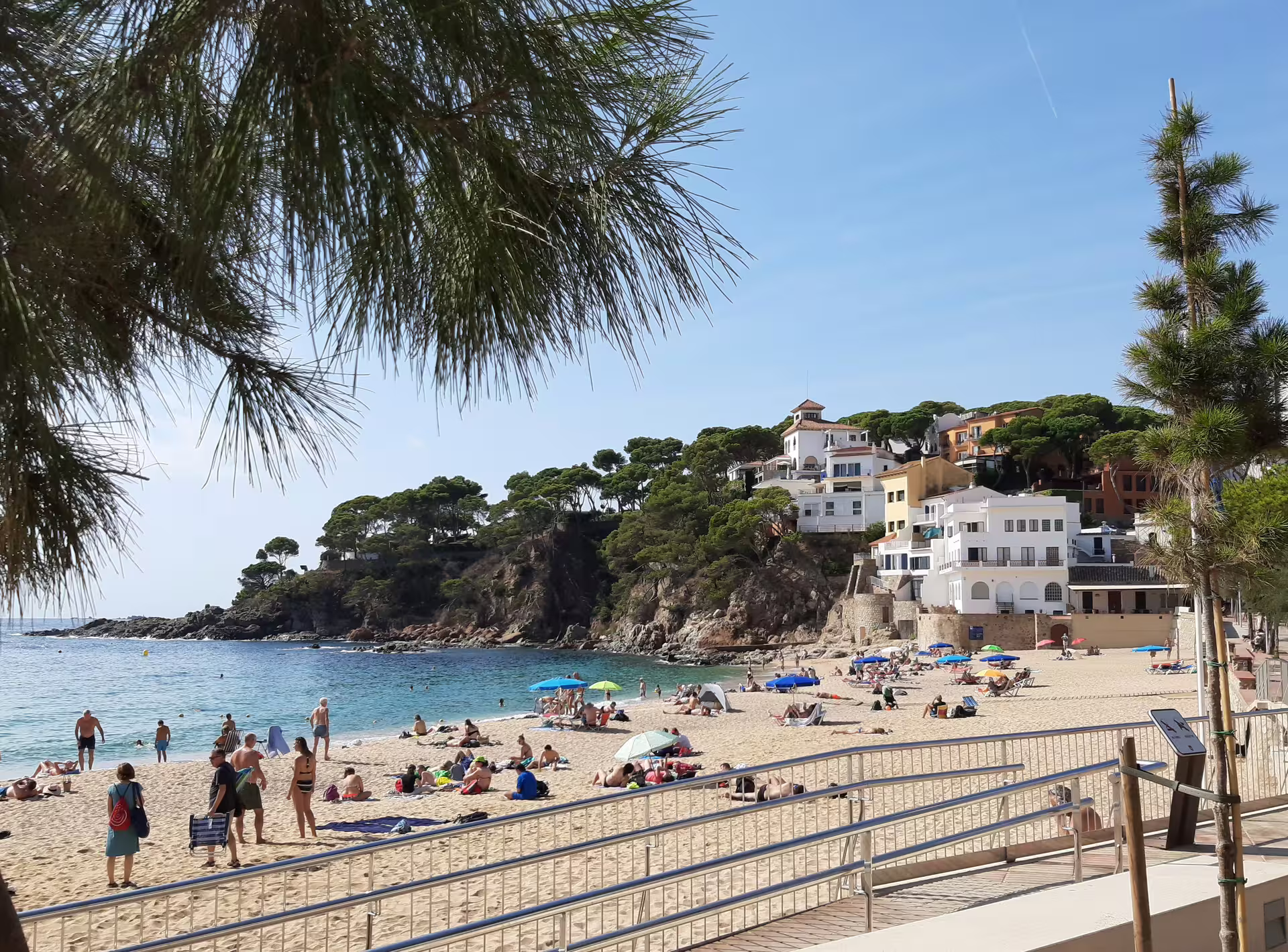 Sunny beach scene in Costa Brava with people enjoying the sandy shore and picturesque cliffs in the background.