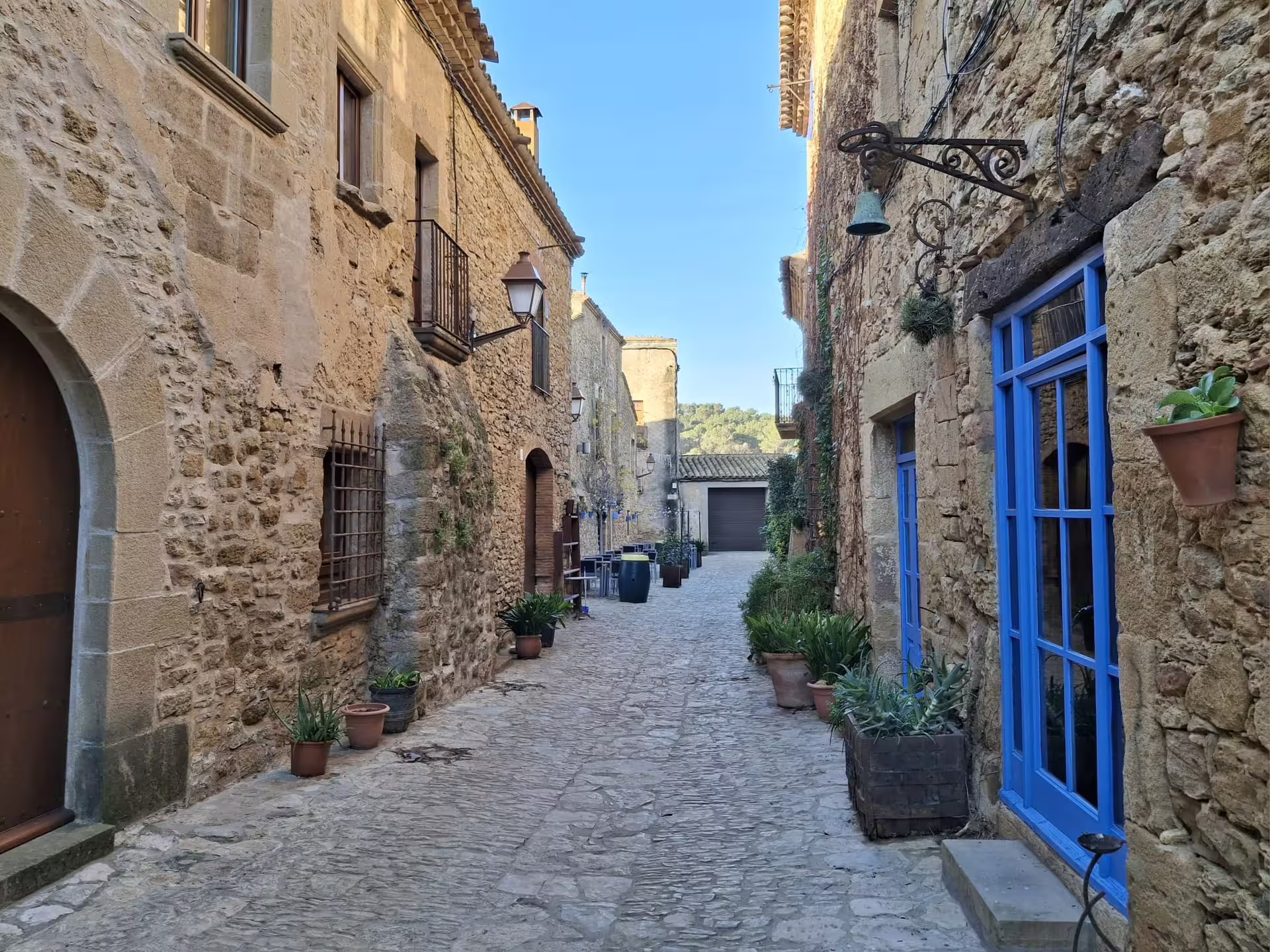 Charming cobblestone street in a typical Costa Brava town with rustic stone buildings and vibrant blue accents.
