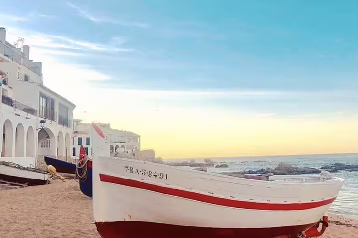 Traditional fishing boats on the sandy shore of Costa Brava, with a picturesque sunset over the sea.