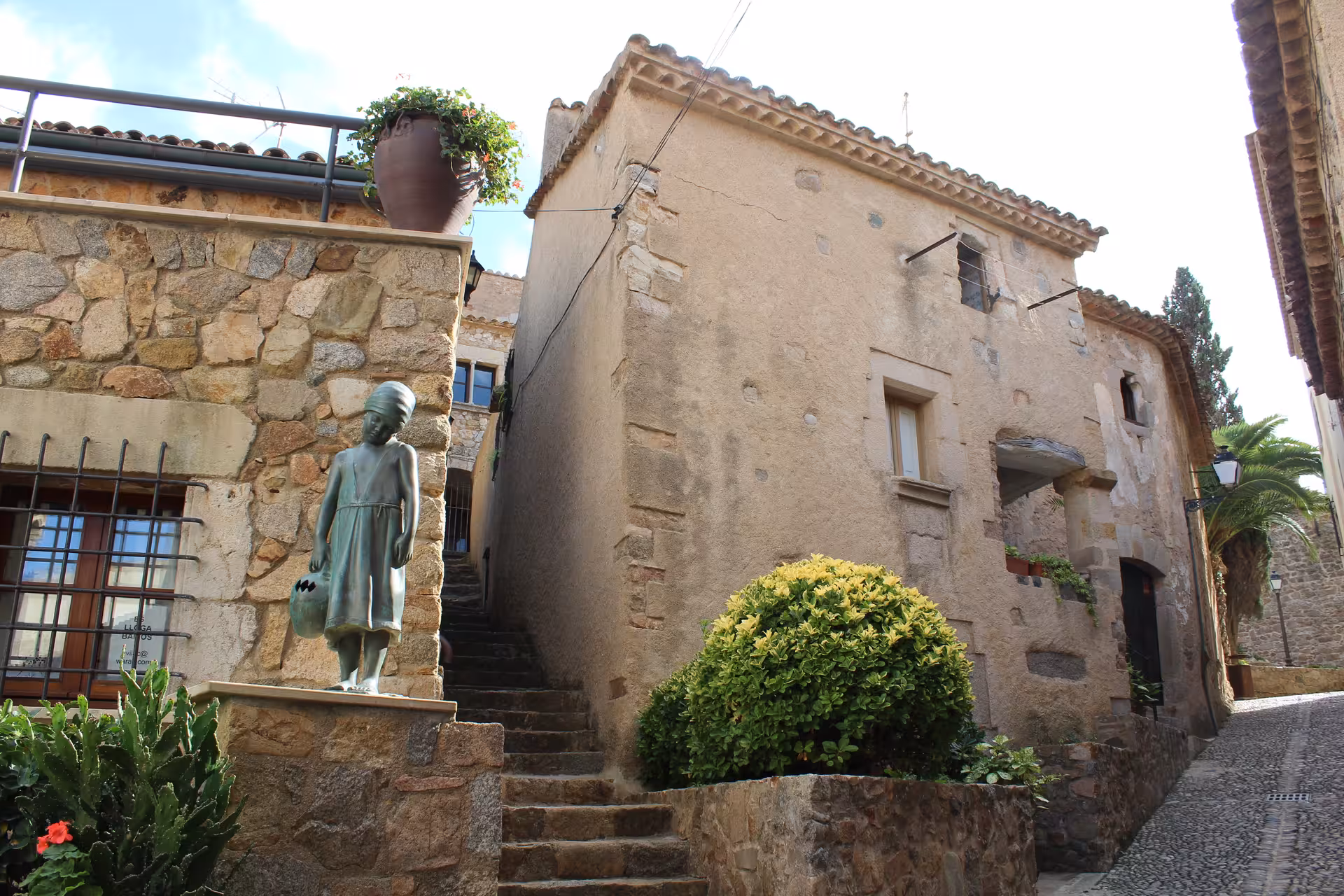 Medieval Costa Brava village street stop on beach trip from Barcelona, stone houses, steps and sculpture