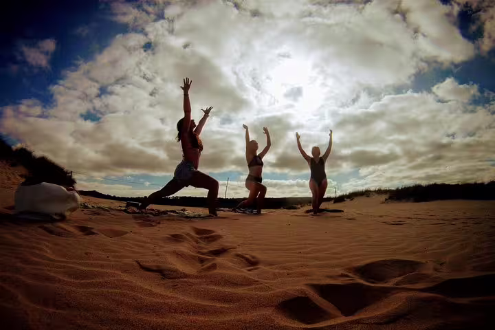 People practicing yoga on a sandy beach at Costa da Caparica under a dramatic cloudy sky, perfect for a surf and yoga retreat.
