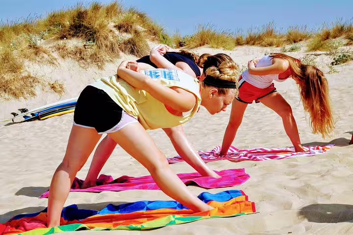 Women practicing yoga on sandy Costa da Caparica beach, part of a surf and yoga retreat near Lisbon under clear blue skies.