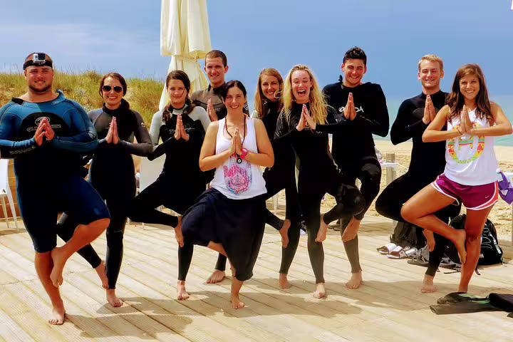 Group enjoying yoga in wetsuits on Costa da Caparica beach, blending surf and mindfulness near Lisbon.