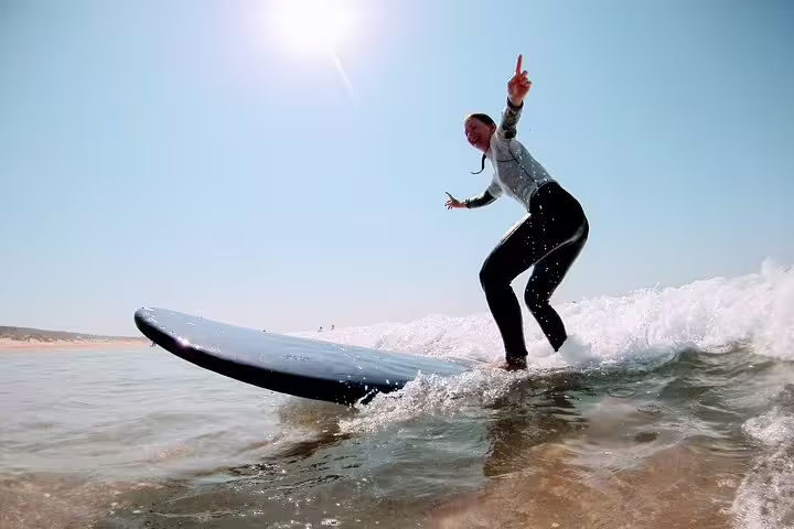 A woman surfs a wave under the sun at Costa da Caparica, showcasing a vibrant surf and yoga experience near Lisbon.