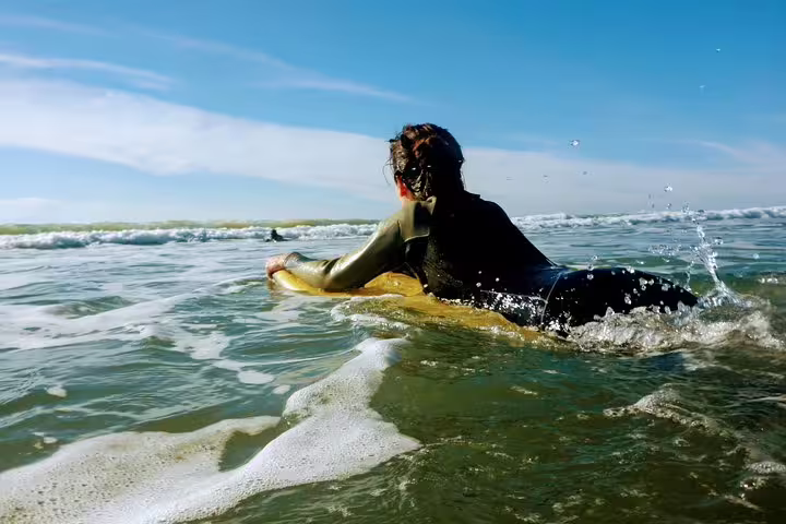 Surfer in a wetsuit paddling on a board in sunny Costa da Caparica, ideal for a surf and yoga retreat from Lisbon.