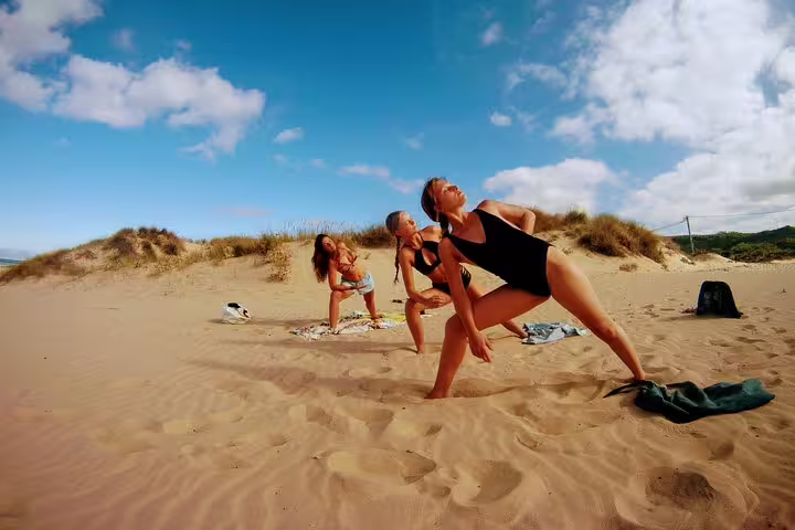 Women practicing yoga on sandy Costa da Caparica beach under clear blue skies, part of Lisbon's surf and yoga retreat.