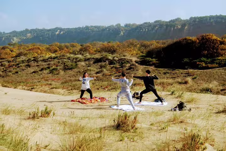 Participants practicing yoga on sandy dunes with lush greenery in Costa da Caparica, ideal for a Lisbon surf and yoga retreat.