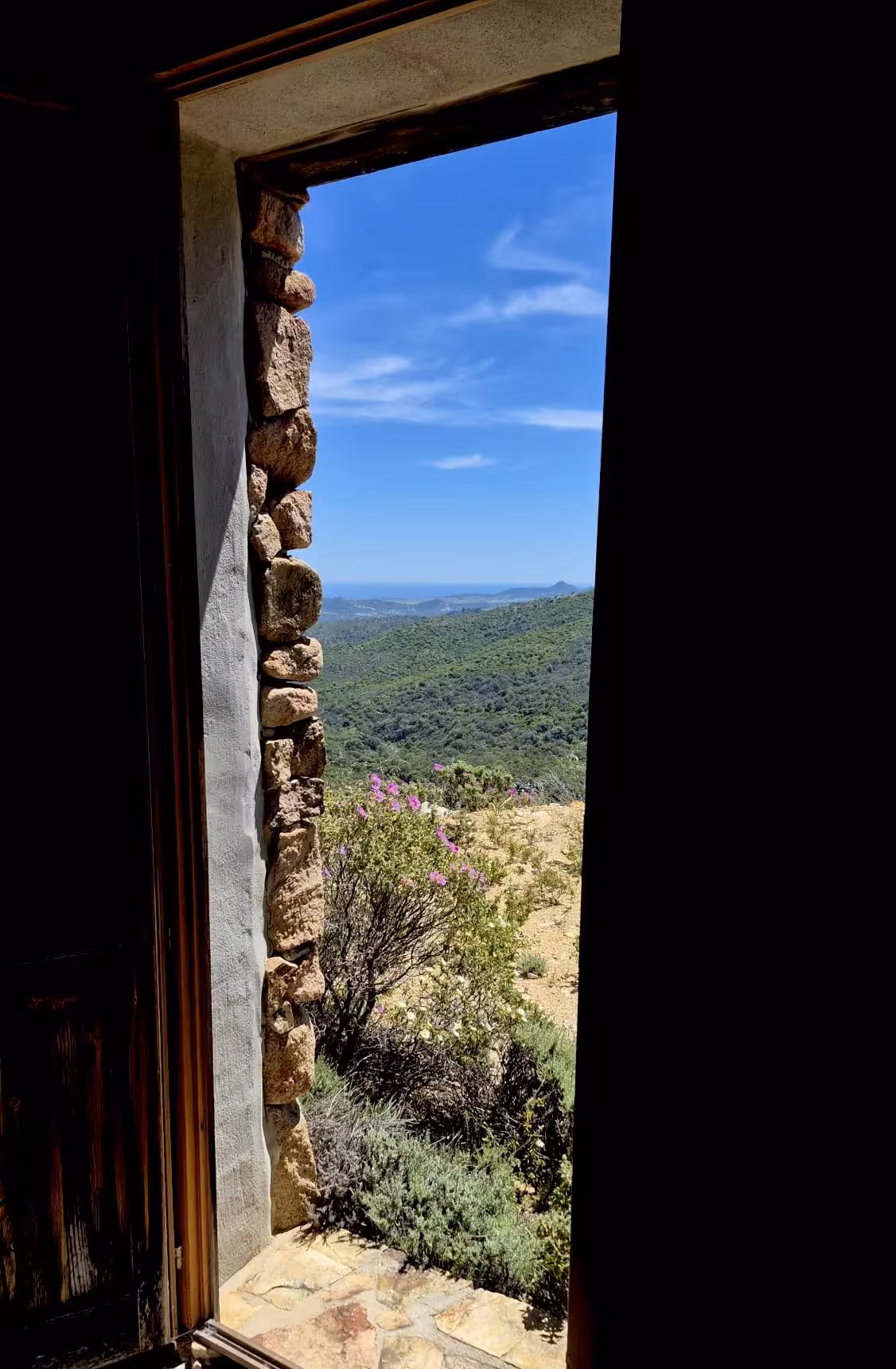 Breathtaking view of Costa Rei's lush landscape from a rustic stone doorway under a clear blue sky.