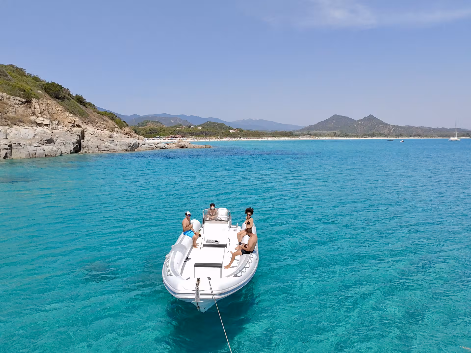 Private dinghy on crystal-clear turquoise waters near Costa Rei, surrounded by scenic coastal cliffs.