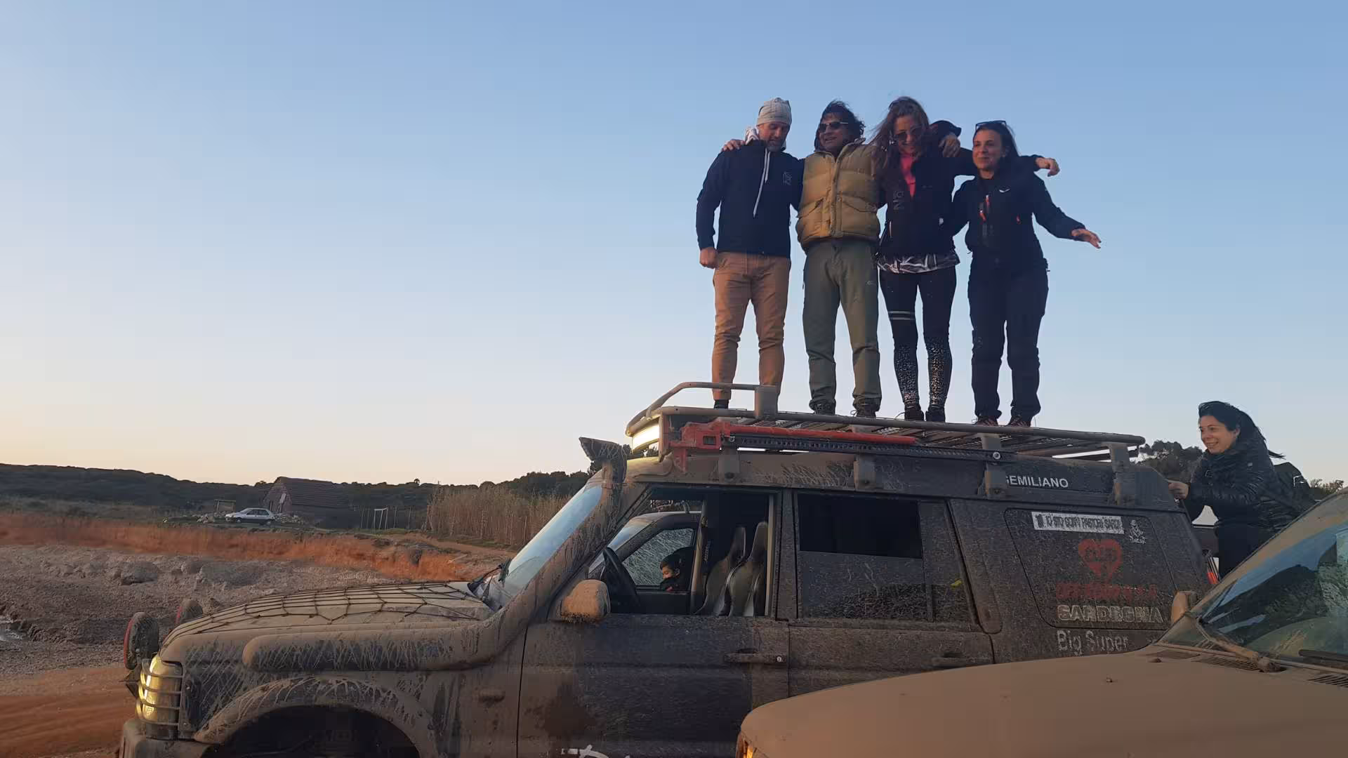 Tourists stand atop a 4x4 vehicle enjoying the sunset on a Costa Verde off-road adventure from Oristano.