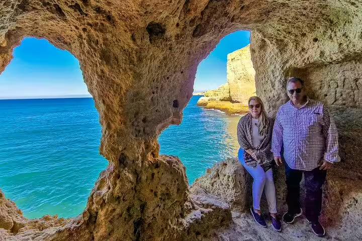 Couple enjoying stunning Algarve coastal views from a rocky cave in Algar Seco during a private 2-day tour from Lisbon, Portugal.