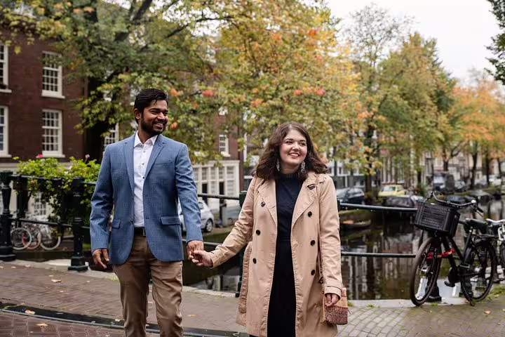 Smiling couple strolling beside an Amsterdam canal in autumn, shot on a personal travel photographer tour