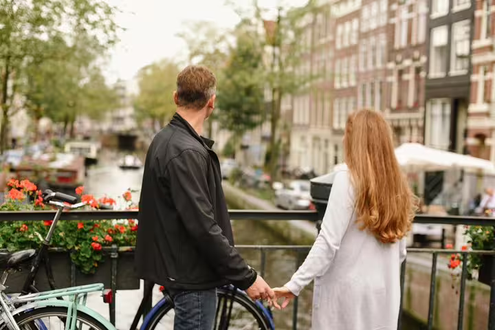 Couple holding hands on an Amsterdam canal bridge, romantic vacation photoshoot with a personal travel photographer