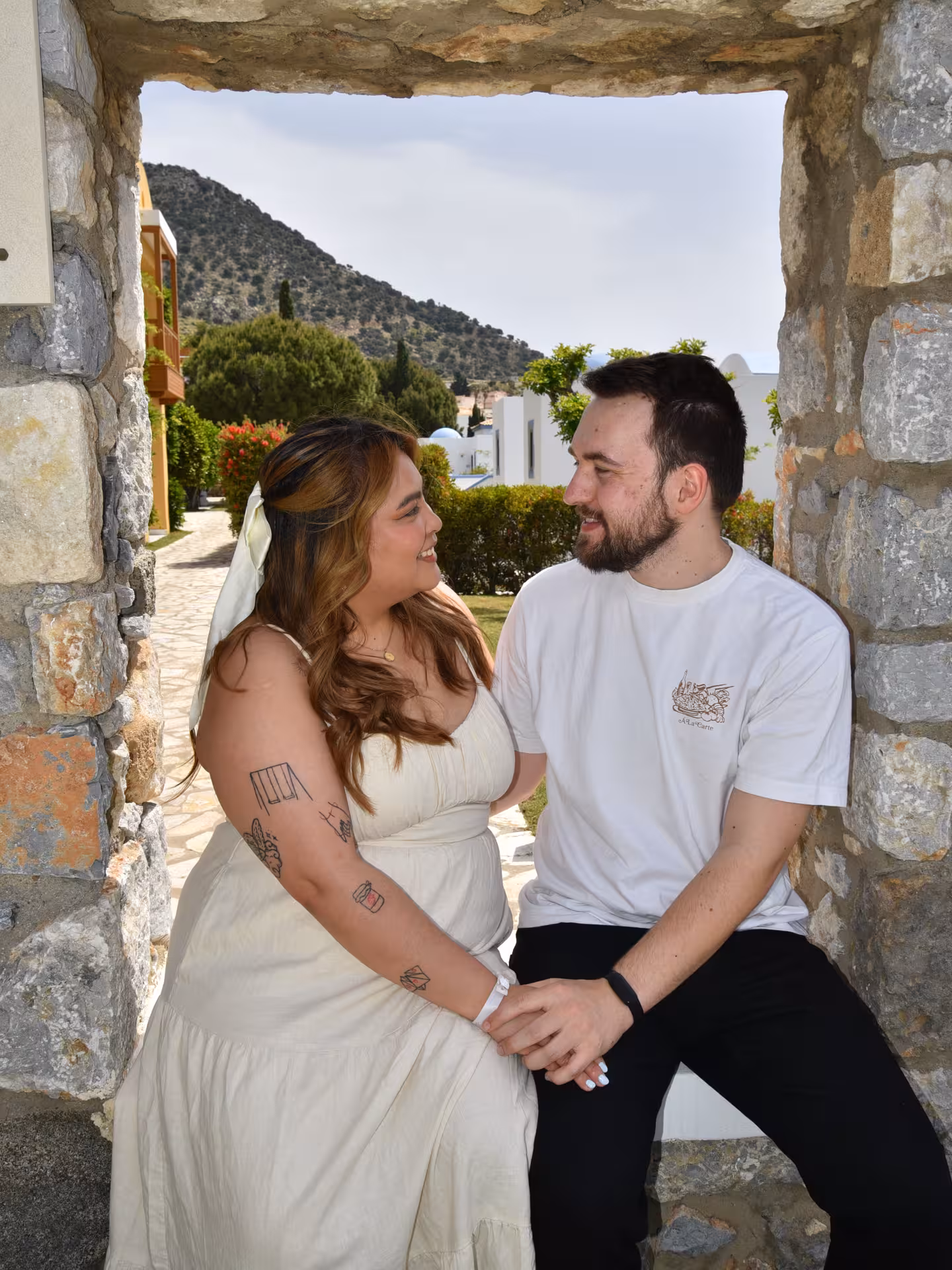 Couple sharing a romantic moment at Heraklion Venetian Port, framed by a stone archway with scenic mountain backdrop.
