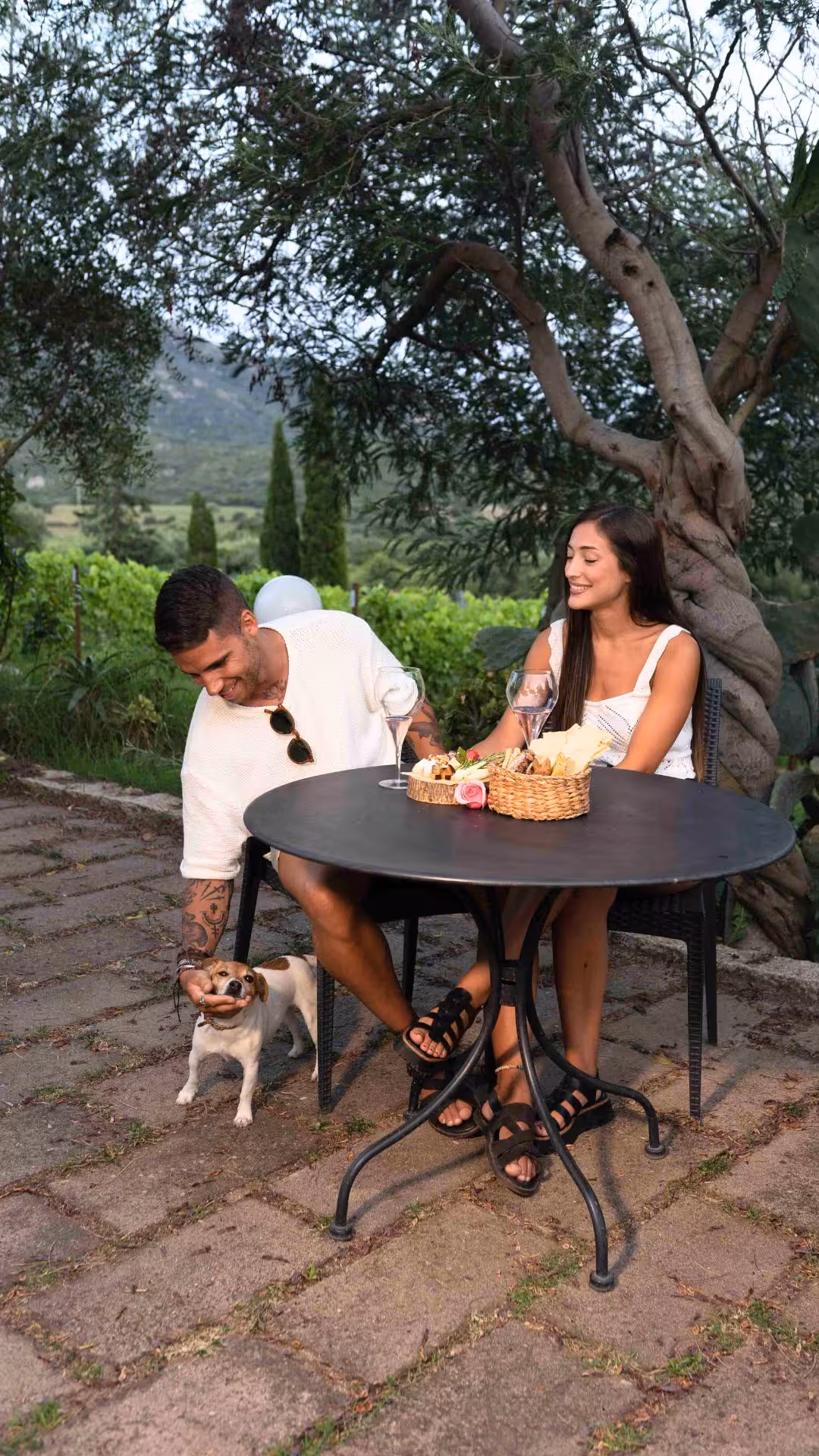 Couple relaxing with aperitif and a small dog at a Gallura winery in Olbia.
