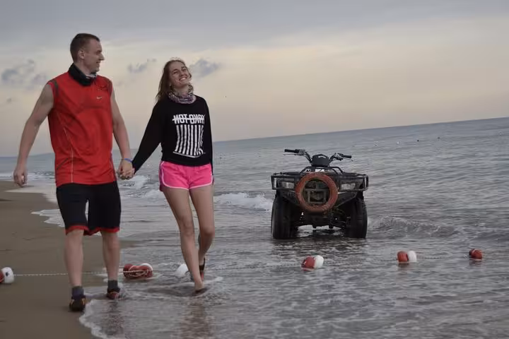 Couple walking by the sea beside an ATV on Antalya beach, part of a Quad Safari coastal ride experience
