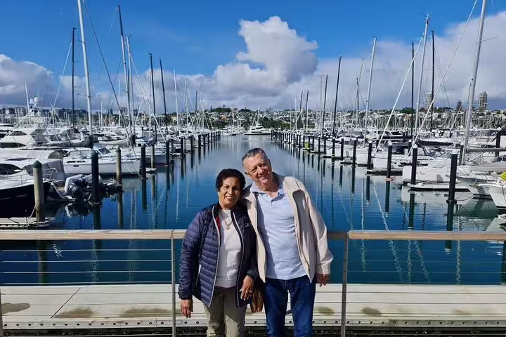 Couple standing by a bustling marina filled with yachts, enjoying the Private Auckland Highlight Day Tour.