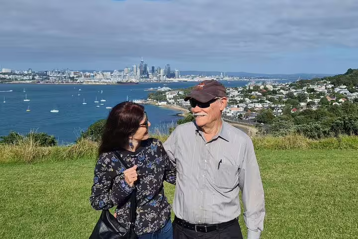 Couple enjoying scenic view of Auckland skyline and harbor from a grassy hilltop during a private day tour.