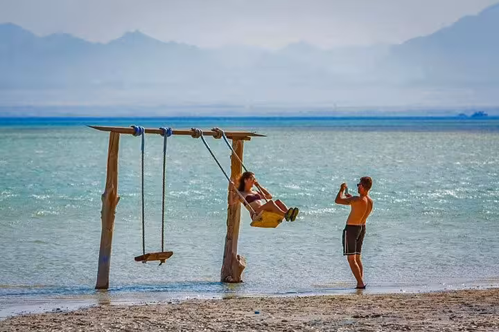 Couple enjoying beach swing at Orange Bay Giftun Island, Hurghada snorkeling tour with crystal Red Sea views