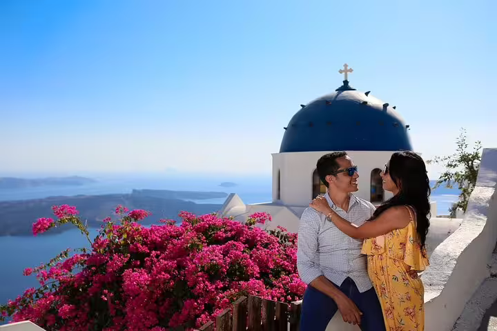 Couple embraces by blue dome church in Oia, Santorini, for a surprise proposal photoshoot with photographer