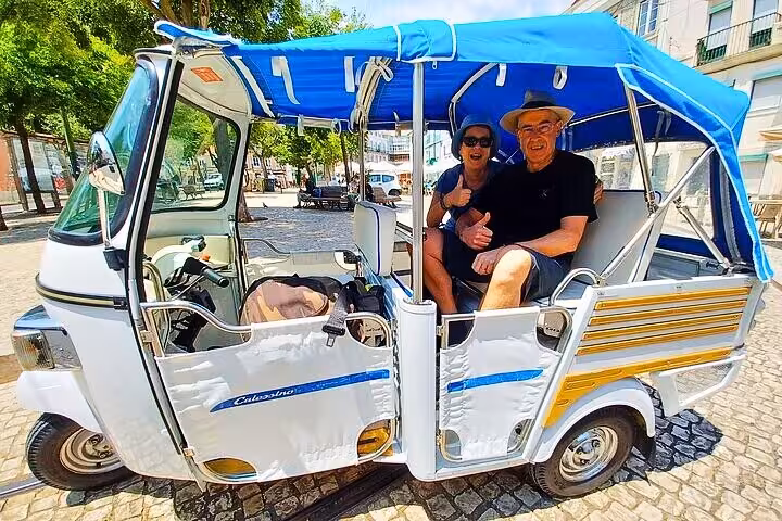 Smiling couple in a blue-roof tuk tuk on a 4-hour private Lisbon tour, exploring historic neighborhoods