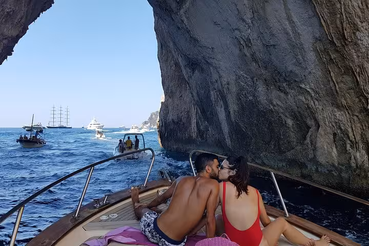 Couple sharing a kiss on boat near Capri Island, surrounded by scenic cliffs and clear Mediterranean waters.