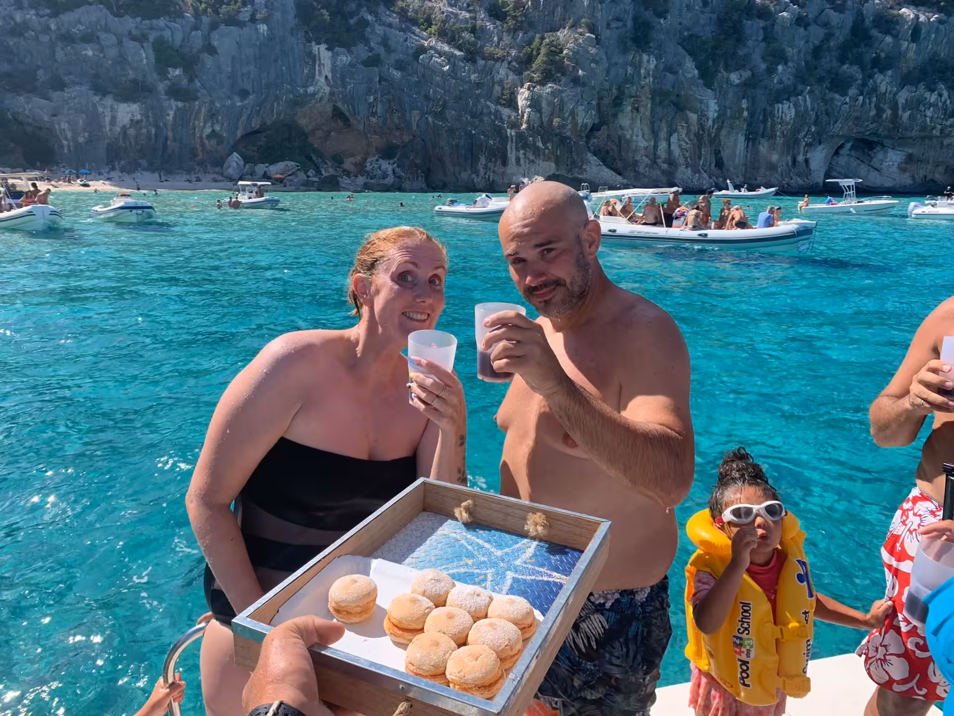 Smiling couple enjoying refreshments on a boat tour in the stunning Gulf of Orosei, surrounded by clear blue waters.