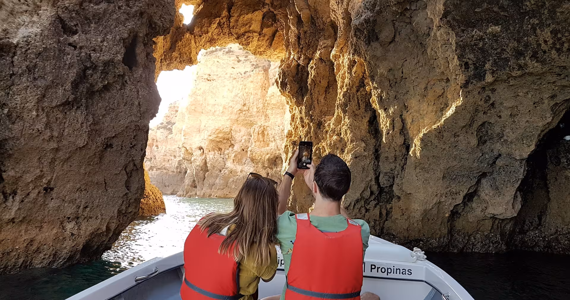 Couple in life jackets on boat tour photographing golden sea caves and arches of Ponta da Piedade in Lagos, Algarve coast