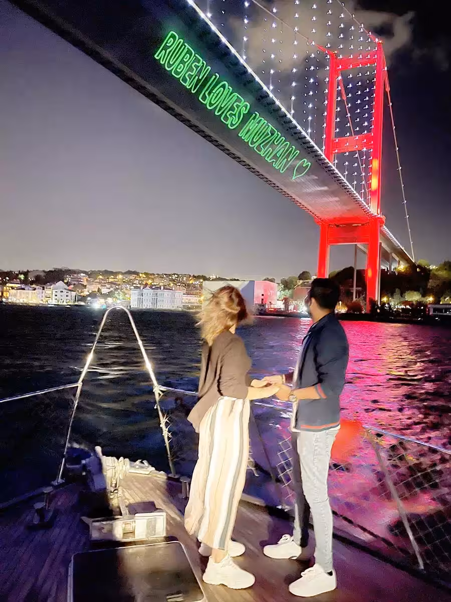 Couple holding hands on a private Bosphorus yacht cruise under the bridge lights, romantic marriage proposal tour