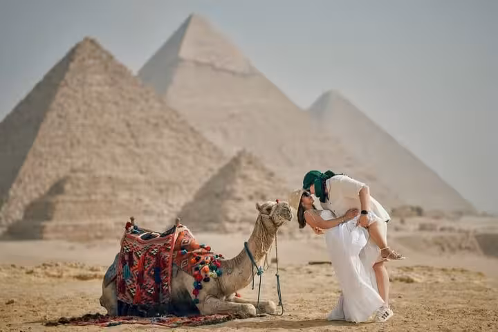 Couple by a decorated camel with the Giza Pyramids backdrop on a full-day Cairo tour with pickup