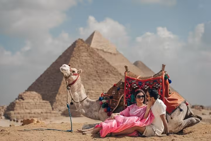 Couple resting beside decorated camel with Pyramids of Giza behind on private Giza pyramids tour, Cairo