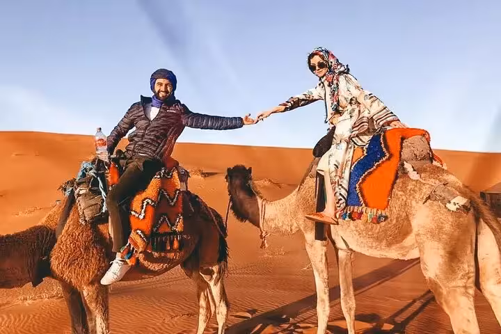 Couple enjoying a camel ride in the stunning landscape of Merzouga Desert, sharing a joyful moment.