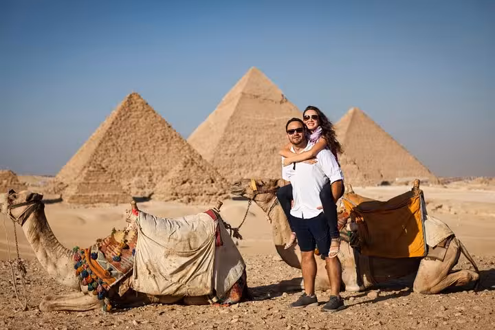 Couple with camels at Giza Pyramids desert viewpoint on Cairo tour including Sphinx and Grand Egyptian Museum