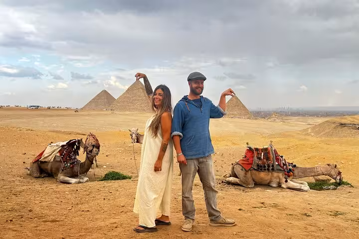 Couple posing with camels at Giza Pyramids on skip-the-line hidden gems tour, epic perspective photo