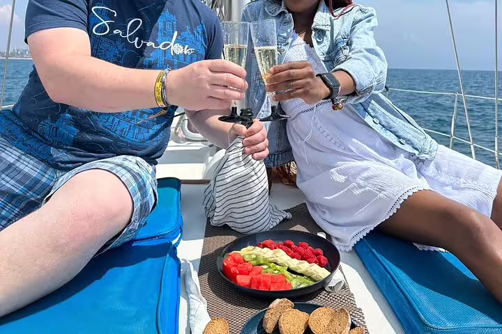 Couple toasting with champagne on a sailboat deck with fresh fruit and snacks, enjoying a scenic Ibiza and Formentera tour.