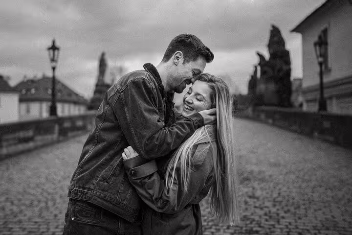 Black and white photo of a couple sharing a joyful moment on the iconic Charles Bridge in Prague.