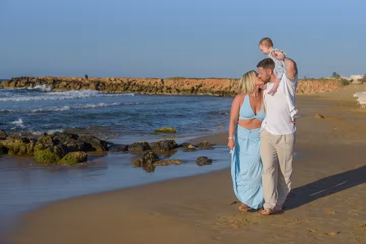 Couple with a child walking along a scenic Heraklion beach during a private photoshoot, surrounded by waves and rocks.
