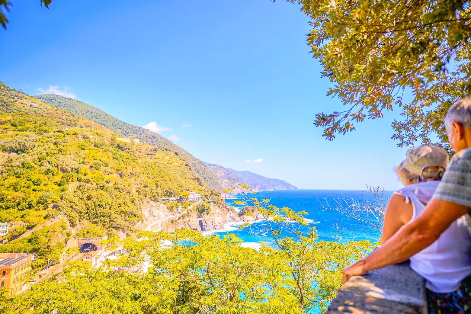 Couple admiring scenic coastal view with lush hills and blue sea in Cinque Terre, Italy.
