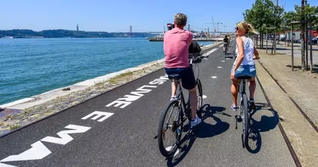 Couple cycling along Lisbon's scenic waterfront path with views of the Tagus River on a French bike tour.