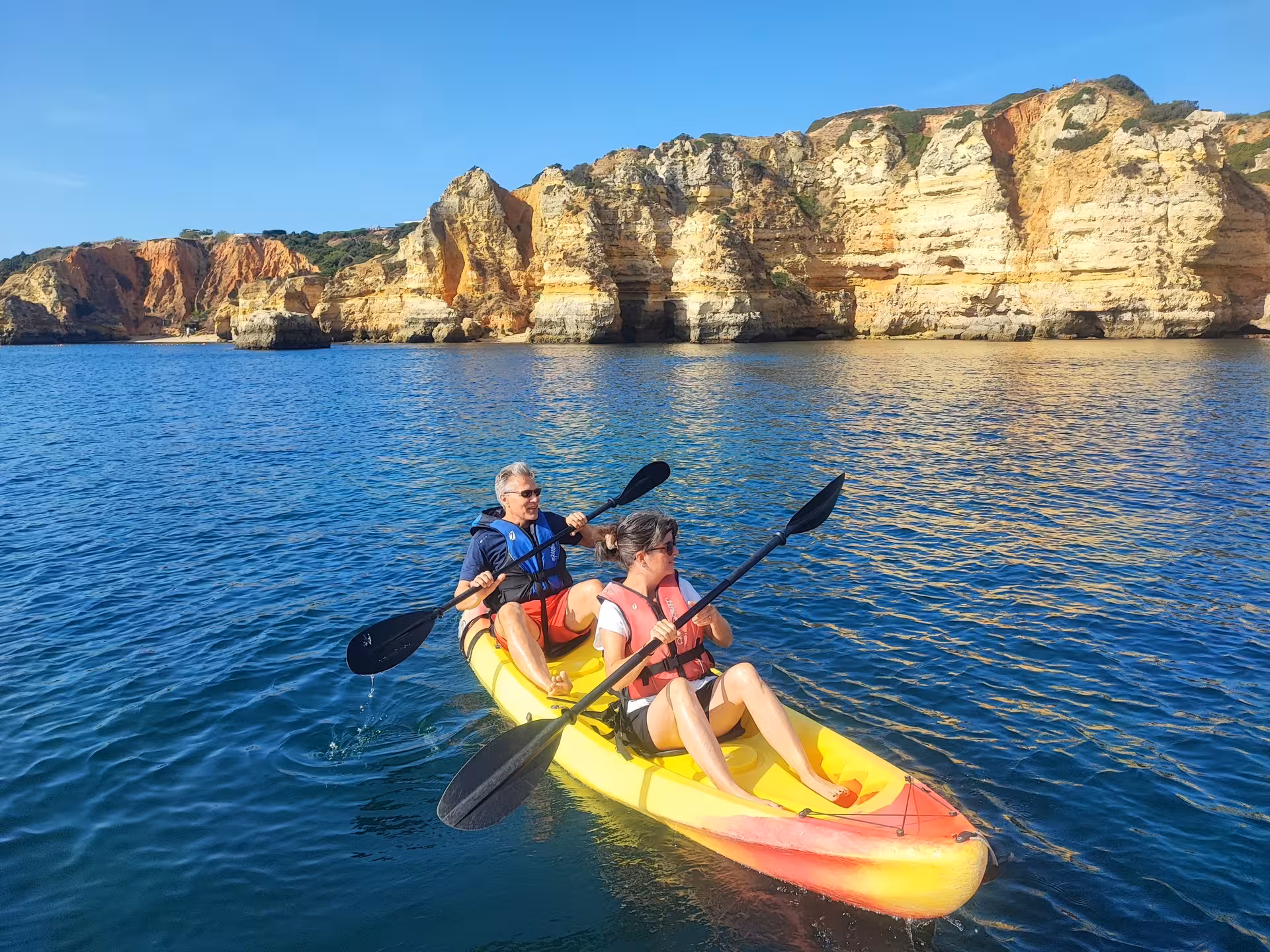 Couple enjoying a scenic double kayak rental on calm blue ocean waters beneath dramatic Algarve rock formations in Portugal