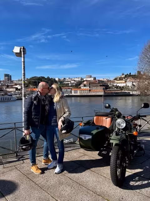 Couple by the Douro River with vintage sidecar motorbike on a Porto morning tour, Ribeira skyline view