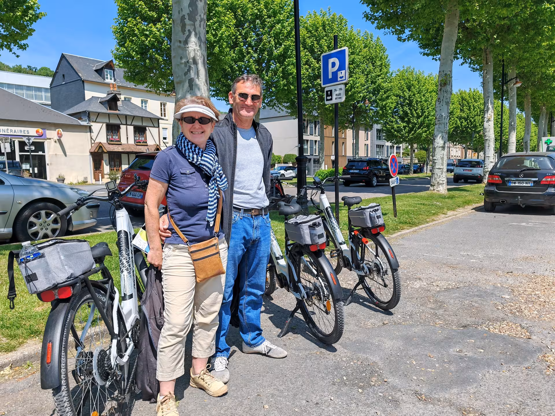 Couple posing with e-bikes on a guided electric bike tour of Honfleur, Normandy, on a sunny tree-lined street
