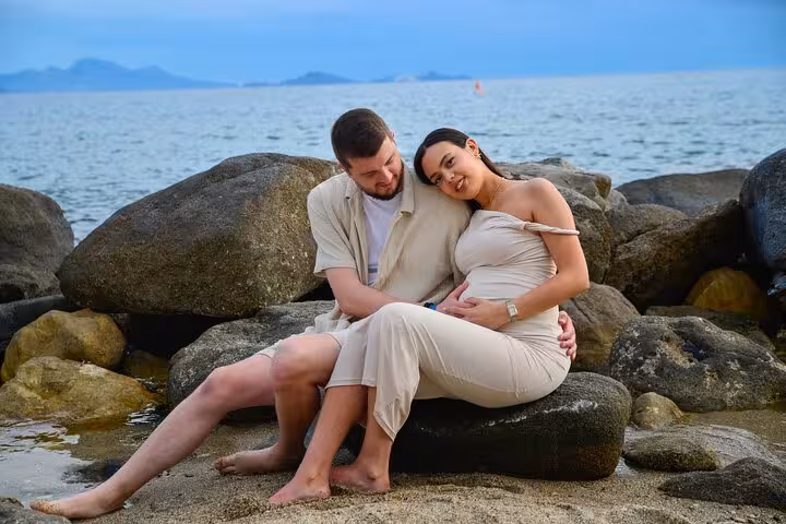 A couple lovingly embraces on a rocky beach, with a serene ocean view in Analipsi, capturing a tender moment.