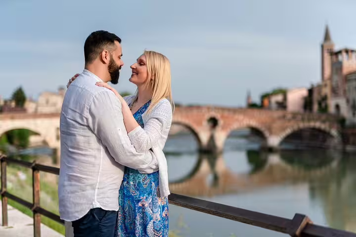 Couple embracing by the Adige River with Verona's historic bridge in the background, perfect for romantic photoshoots.