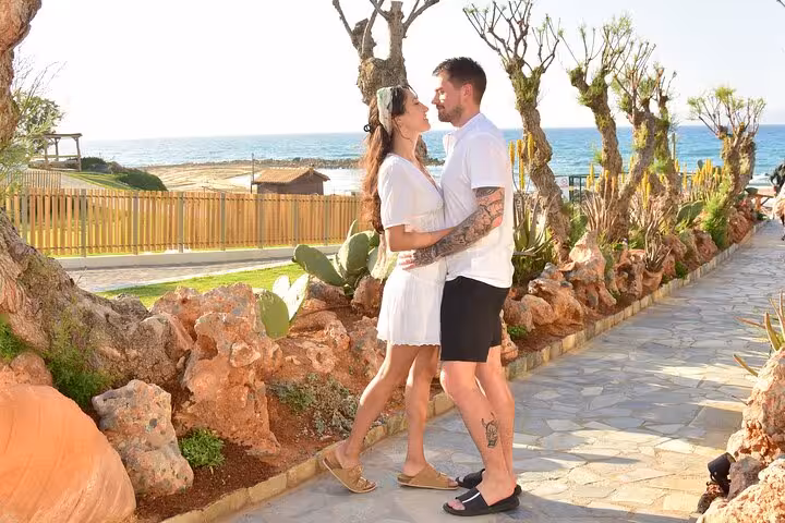 Couple embracing on a scenic seaside path in Hersonissos during a private photoshoot, with ocean views in the background.