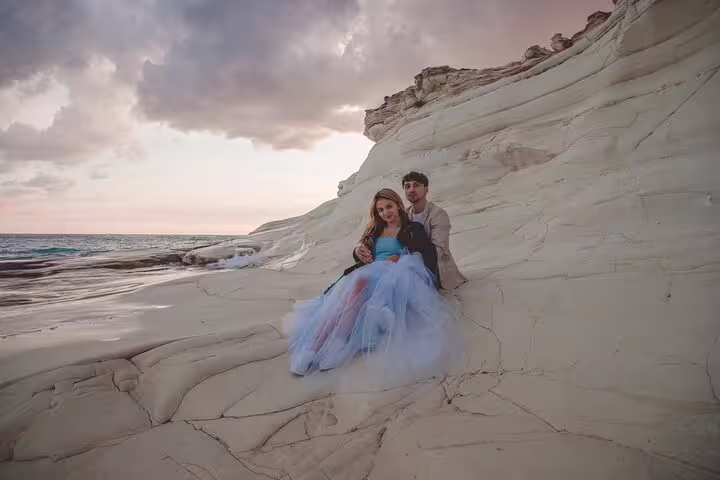 Couple in formal attire embrace on the stunning rocky coast of Ayia Napa during a sunset photoshoot.