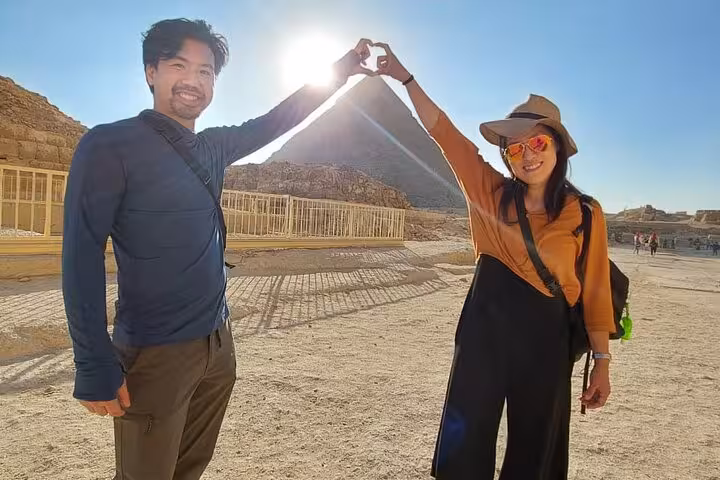 Couple making a heart shape with hands at Giza Pyramids during Cairo Airport private day trip with guide