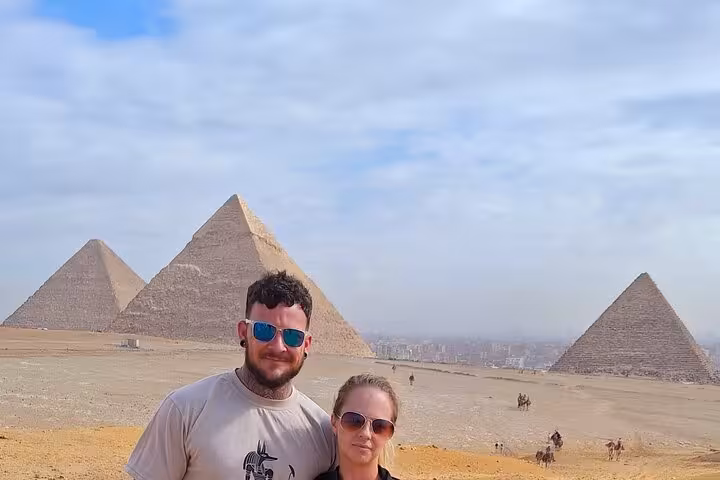 A couple stands with the majestic Giza Pyramids in the background, capturing a memorable moment on their Cairo tour.